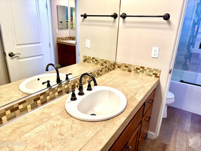 full bathroom with toilet, bath / shower combo with glass door, wood finished floors, vanity, and decorative backsplash