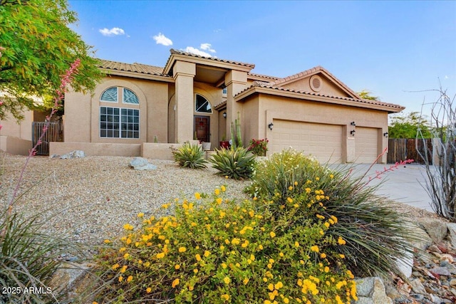 mediterranean / spanish house with a tile roof, concrete driveway, fence, an attached garage, and stucco siding