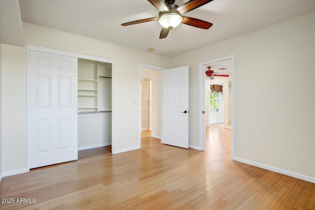 unfurnished bedroom with light wood-style flooring, arched walkways, baseboards, a ceiling fan, and a closet