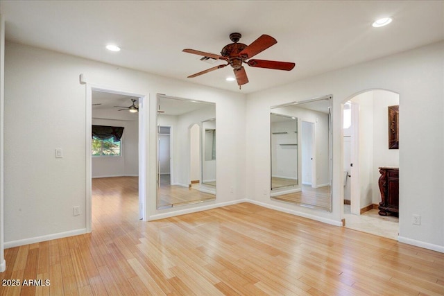 unfurnished room featuring arched walkways, light wood-type flooring, and a ceiling fan