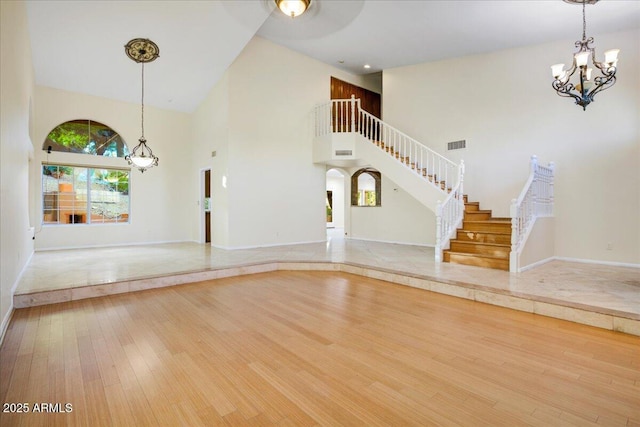 unfurnished living room with visible vents, a chandelier, wood finished floors, a high ceiling, and stairs