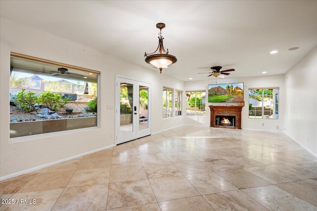 unfurnished living room with recessed lighting, a ceiling fan, french doors, baseboards, and a lit fireplace
