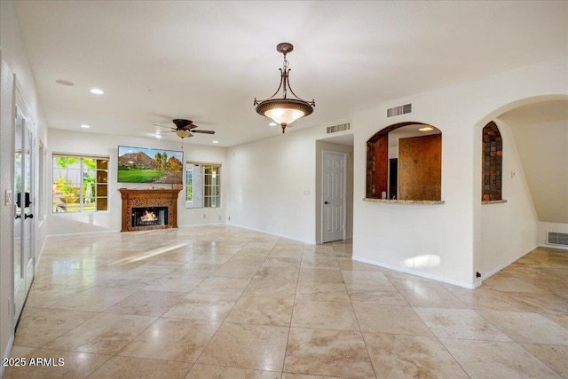 unfurnished living room featuring a warm lit fireplace, baseboards, a ceiling fan, and visible vents