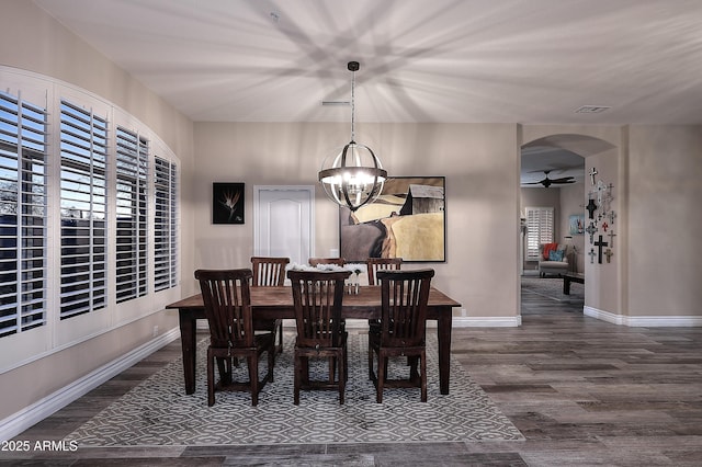 dining space featuring baseboards, arched walkways, dark wood-style flooring, and ceiling fan with notable chandelier