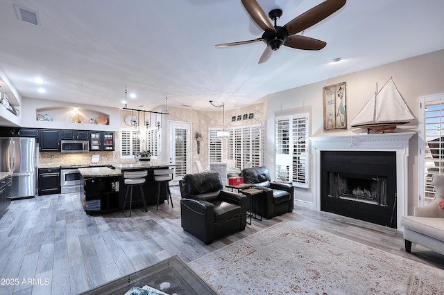 living room featuring ceiling fan, light wood-style flooring, a fireplace, and visible vents