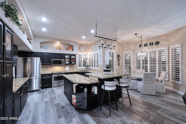 kitchen with stainless steel appliances, a spacious island, a kitchen breakfast bar, hanging light fixtures, and glass insert cabinets