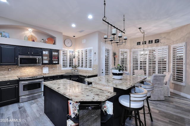 kitchen featuring glass insert cabinets, a center island, stainless steel appliances, pendant lighting, and a notable chandelier