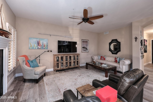 living room featuring a ceiling fan, visible vents, baseboards, and wood finished floors