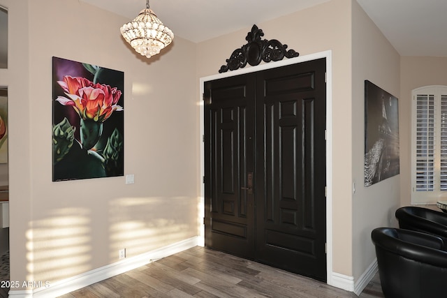 foyer entrance featuring an inviting chandelier, baseboards, and wood finished floors