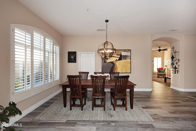 dining area featuring baseboards, visible vents, arched walkways, and wood finished floors