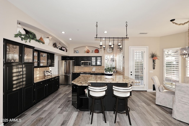 kitchen with decorative backsplash, a kitchen island, appliances with stainless steel finishes, glass insert cabinets, and dark cabinets