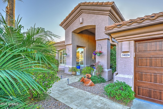 entrance to property with a garage, a tile roof, and stucco siding