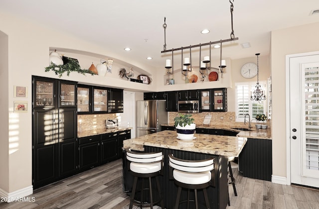 kitchen with pendant lighting, glass insert cabinets, appliances with stainless steel finishes, a kitchen island, and dark cabinets