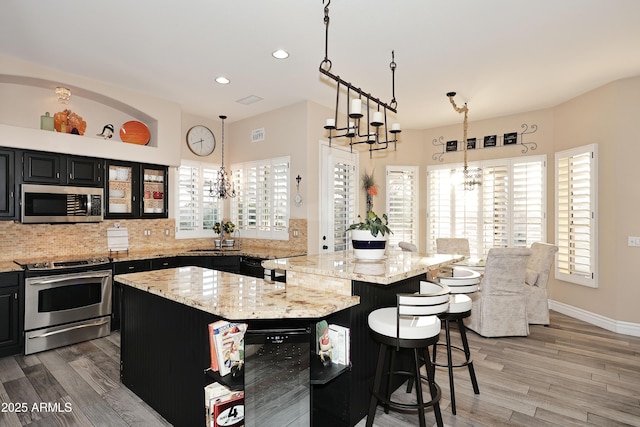 kitchen with appliances with stainless steel finishes, dark cabinetry, a kitchen island, and hanging light fixtures