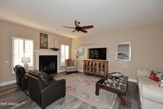 living room featuring ceiling fan, a fireplace, baseboards, and wood finished floors