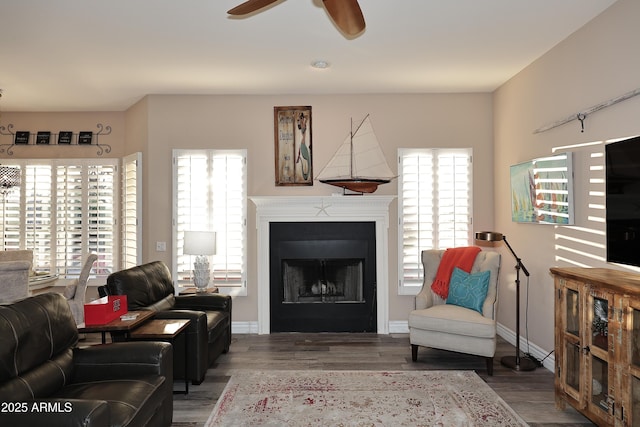 living area with a fireplace, wood finished floors, a ceiling fan, and baseboards