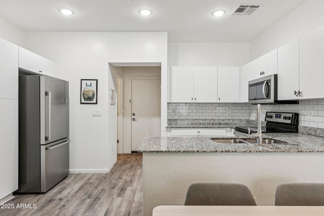 2313 E Hidalgo Ave, Phoenix, AZ 85040 - kitchen with stainless steel appliances, a peninsula, light wood-type flooring, light stone counters, and white cabinetry