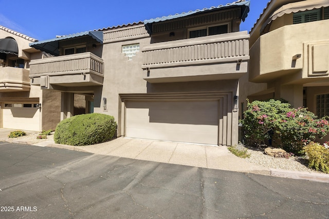 multi unit property with stucco siding, concrete driveway, a balcony, and an attached garage