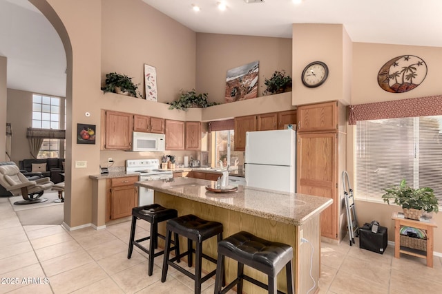 kitchen featuring light tile patterned flooring, a center island, a kitchen breakfast bar, a towering ceiling, and white appliances