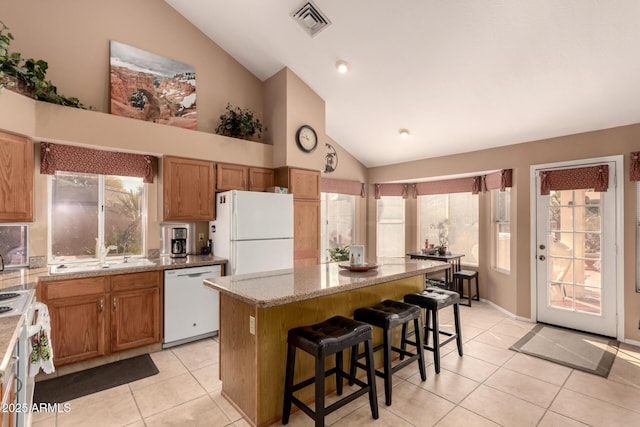 kitchen with a breakfast bar area, light tile patterned floors, a kitchen island, white appliances, and light stone countertops