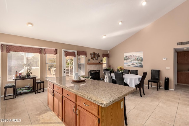 kitchen with light stone countertops, lofted ceiling, a center island, and light tile patterned floors