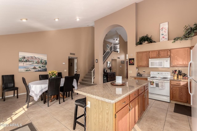 kitchen with a kitchen bar, a center island, high vaulted ceiling, light tile patterned floors, and white appliances