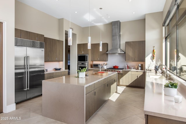 8145 E Tecolote Cir, Scottsdale, AZ 85266 - kitchen featuring built in appliances, a kitchen island with sink, light countertops, wall chimney range hood, and decorative light fixtures