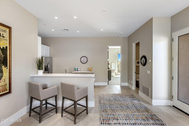 8145 E Tecolote Cir, Scottsdale, AZ 85266 - kitchen with a peninsula, a breakfast bar, white cabinets, light countertops, and stainless steel fridge