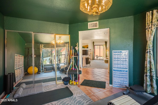 workout area featuring tile patterned flooring, a textured wall, a notable chandelier, and visible vents
