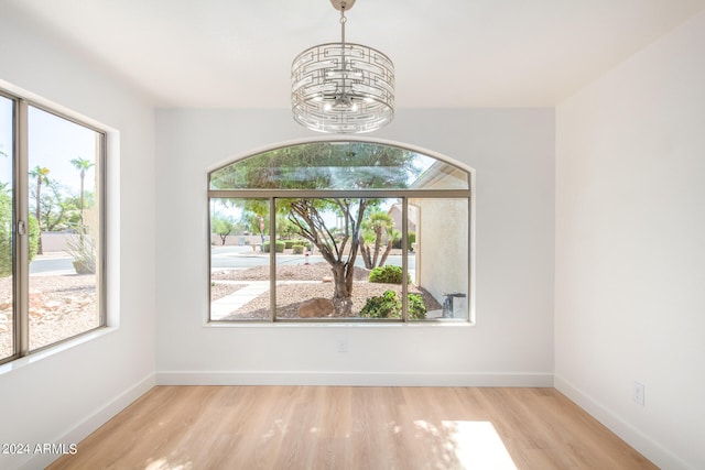 spare room with light hardwood / wood-style floors, a wealth of natural light, and a notable chandelier