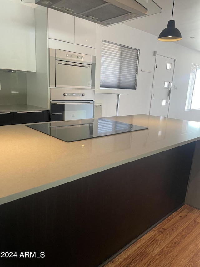 kitchen featuring stainless steel double oven, black electric cooktop, white cabinets, pendant lighting, and light hardwood / wood-style flooring