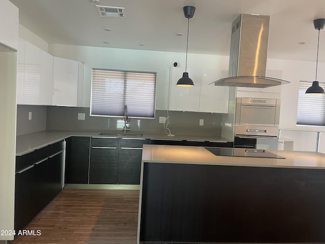 kitchen with island exhaust hood, decorative backsplash, pendant lighting, white cabinets, and sink