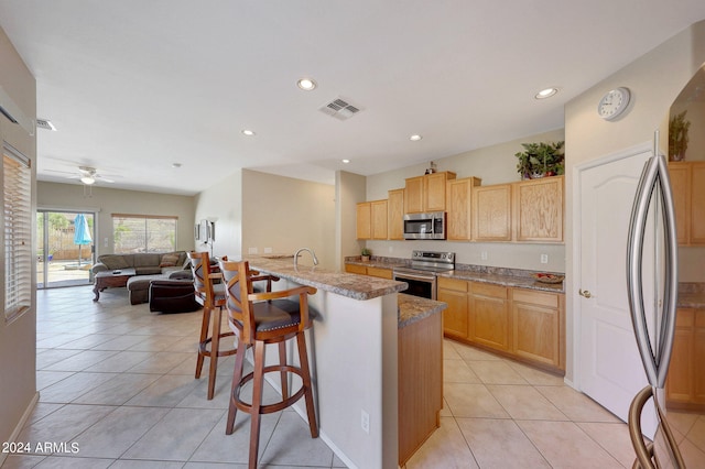 kitchen featuring light tile patterned flooring, a breakfast bar area, stainless steel appliances, light stone countertops, and ceiling fan