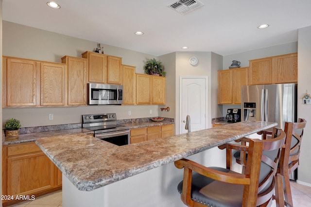 kitchen featuring light stone counters, a breakfast bar, light tile patterned floors, stainless steel appliances, and a center island