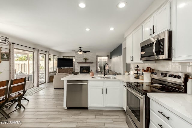 kitchen featuring stainless steel appliances, a peninsula, a sink, a ceiling fan, and open floor plan