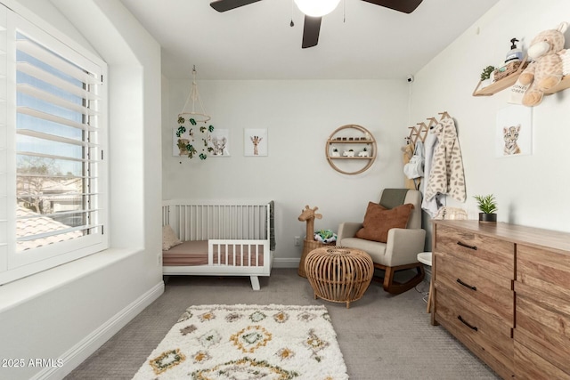 carpeted bedroom featuring a crib, ceiling fan, and baseboards