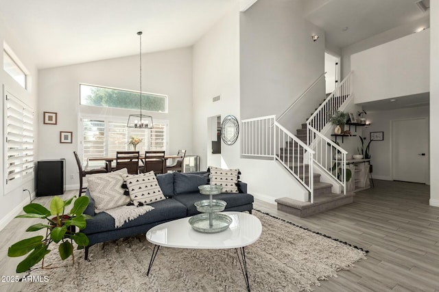 living room featuring visible vents, baseboards, stairway, wood finished floors, and a notable chandelier