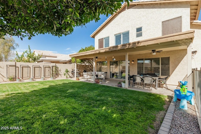 back of house with a yard, a fenced backyard, a ceiling fan, and stucco siding