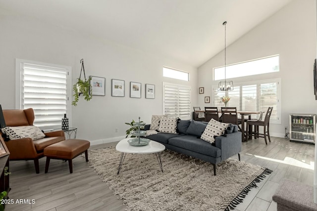 living room with high vaulted ceiling, light wood-type flooring, baseboards, and an inviting chandelier