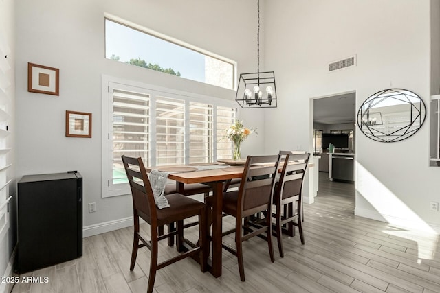 dining room with baseboards, visible vents, a towering ceiling, an inviting chandelier, and light wood-style floors