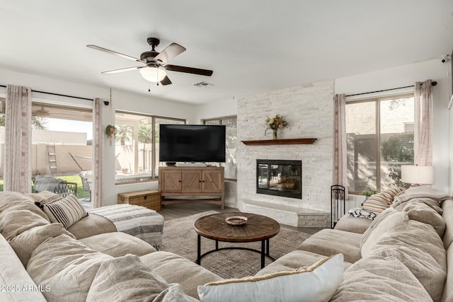 living area with a ceiling fan, wood finished floors, a wealth of natural light, and a stone fireplace