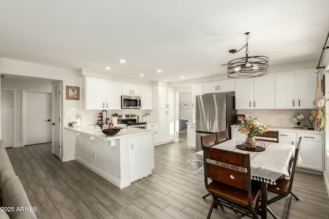 kitchen featuring stainless steel appliances, a peninsula, a sink, white cabinetry, and decorative backsplash