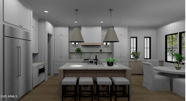 kitchen featuring built in appliances, light stone counters, white cabinets, a center island with sink, and decorative light fixtures