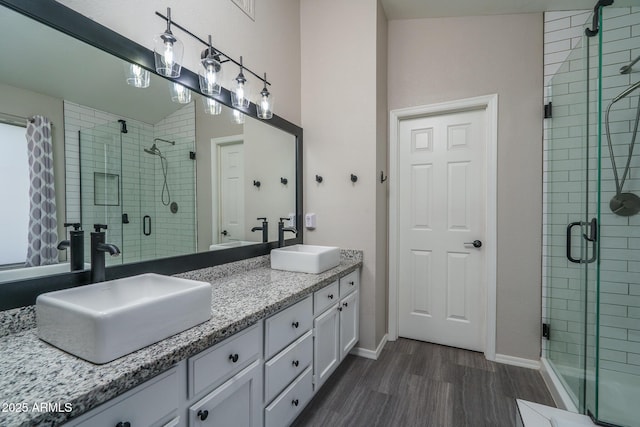 bathroom with a shower stall, wood finished floors, double vanity, and a sink