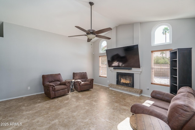 living room with high vaulted ceiling, a ceiling fan, baseboards, and a lit fireplace