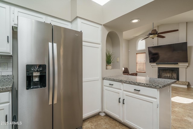 kitchen with a fireplace with raised hearth, open floor plan, stainless steel fridge, a peninsula, and white cabinets