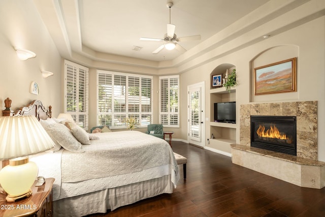 bedroom featuring a premium fireplace, a tray ceiling, access to exterior, baseboards, and wood finished floors