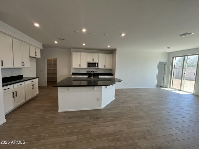 kitchen featuring dark countertops, a sink, stainless steel microwave, visible vents, and recessed lighting