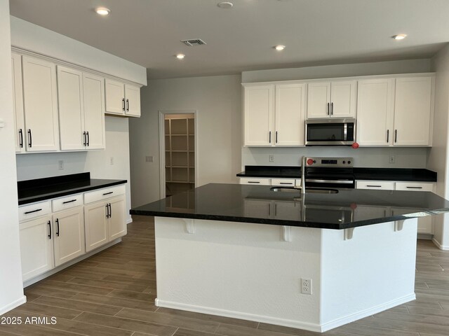 kitchen featuring dark countertops, wood finished floors, white cabinets, appliances with stainless steel finishes, and visible vents
