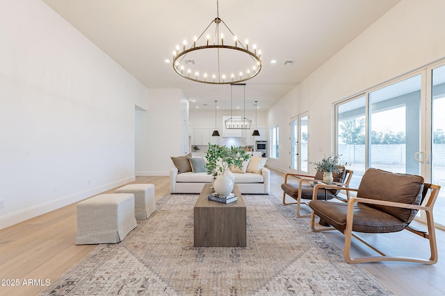 living area with light wood finished floors, a chandelier, visible vents, and baseboards